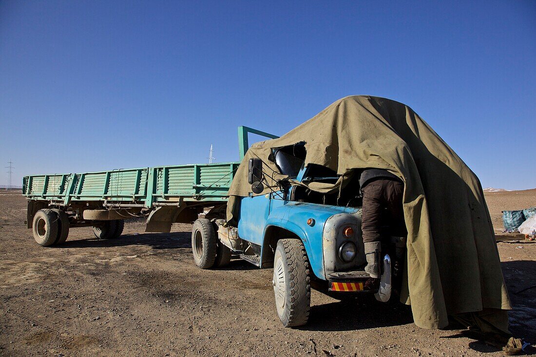 Lastwagenfahrer repariert Motor seines LKWs, wegen der Kälte unter einer Decke, Mongolei