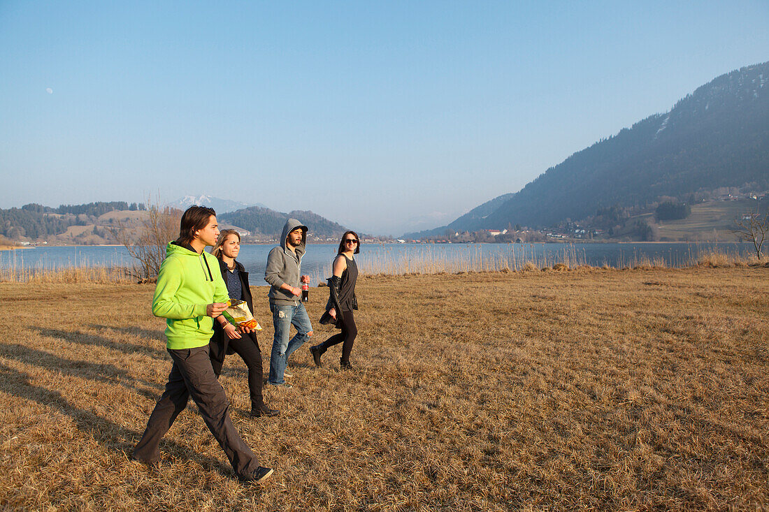 Gruppe junger Leute geht über eine Wiese, Großer Alpsee, Immenstadt im Allgäu, Bayern, Deutschland