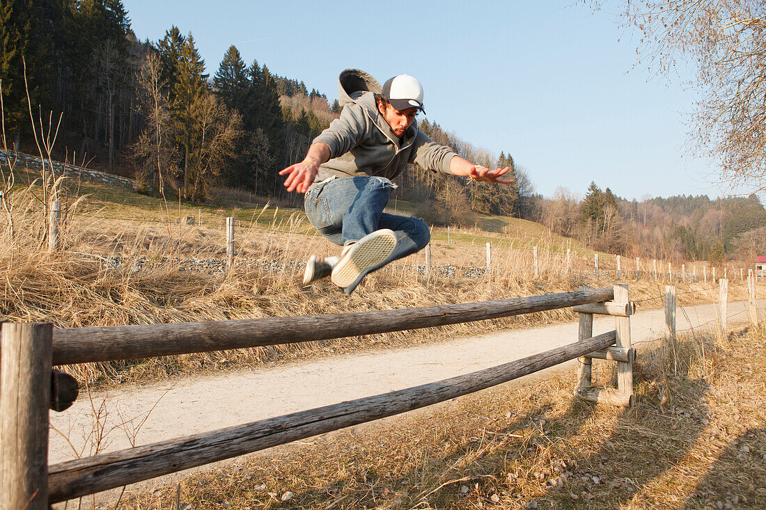 Young man leaping over a fence, Grosser Alpsee, Immenstadt, Bavaria, Germany