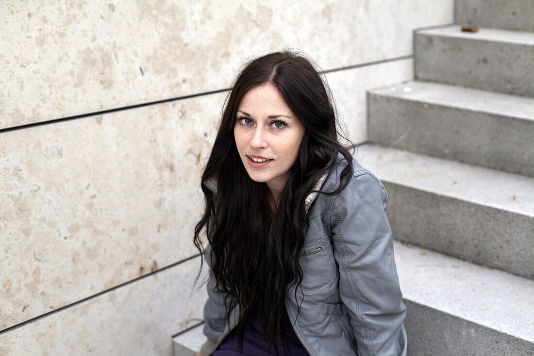 Junge Frau sitzt auf einer Treppe und blickt in die Kamera, München, Bayern, Deutschland