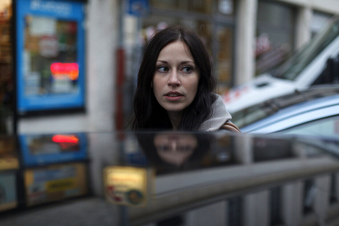 Young woman behind a car, Munich, Bavaria, Germany