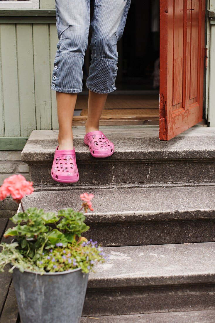 Kind mit pinkfarbenen Schuhen auf Steinstufen vor Haustür und Pflanzenkübel