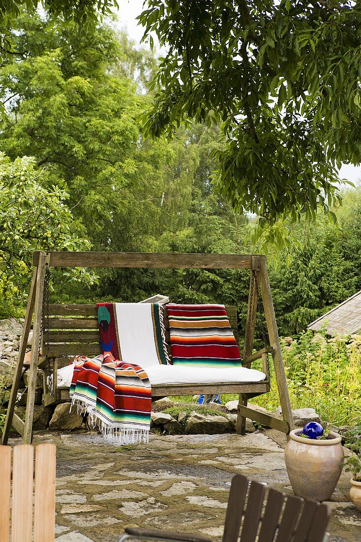 A wooden swing chair with ethnic rugs on a natural stone terrace