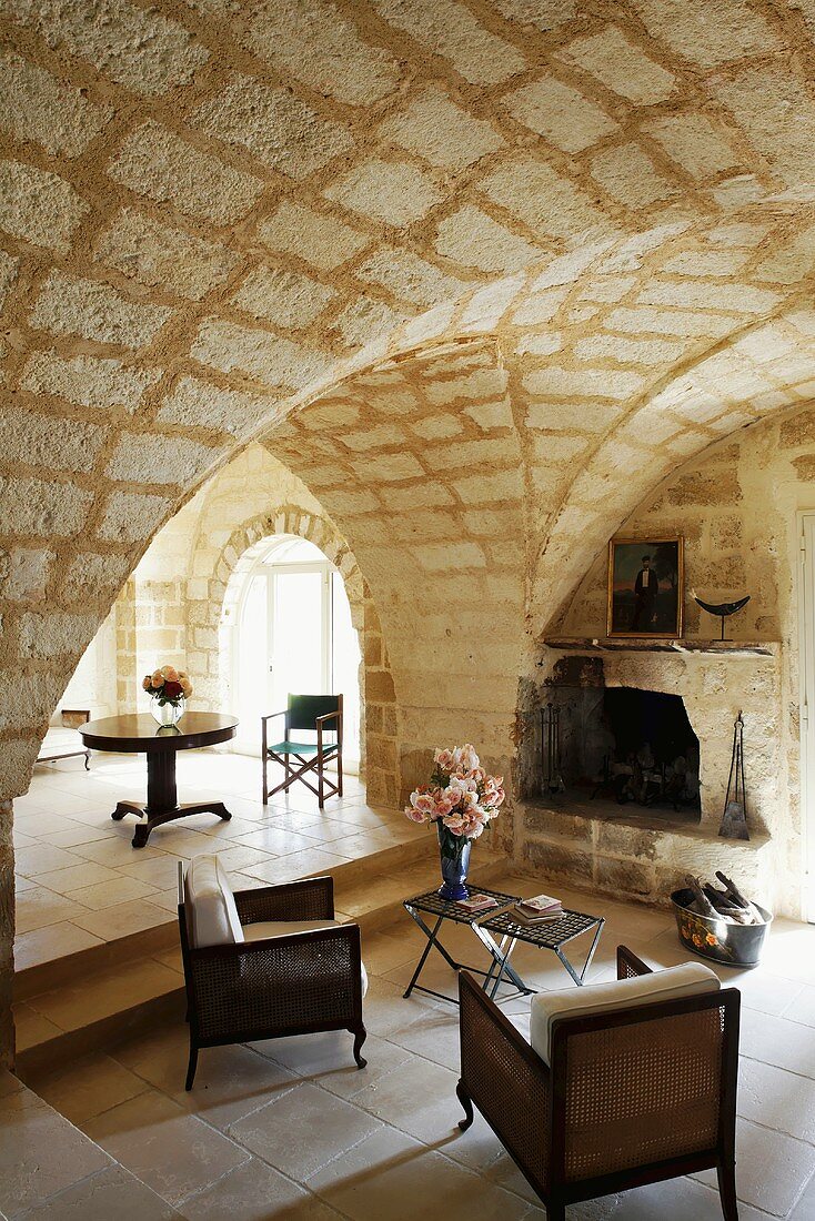 Imposanter Raum mit Kreuzgewölbe aus Natursteinen und Sessel mit Beistelltisch auf Fliesenboden