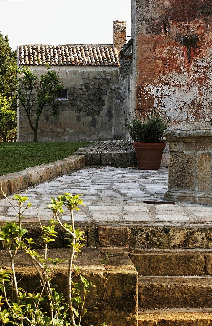 Gepflasterte Terrasse mit Treppe und altes Haus mit Natursteinfassade