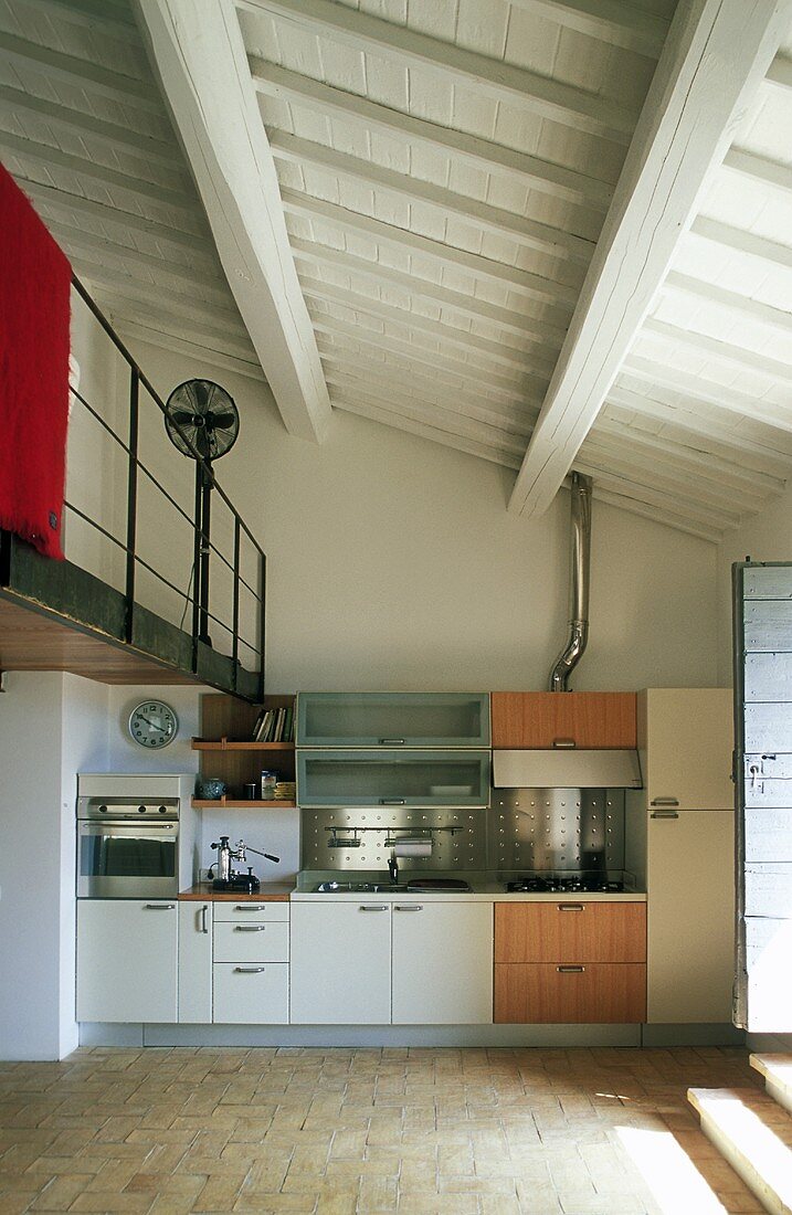 Open kitchen in a living room of a country home with a view of a white beam ceiling painted white and a mezzanine