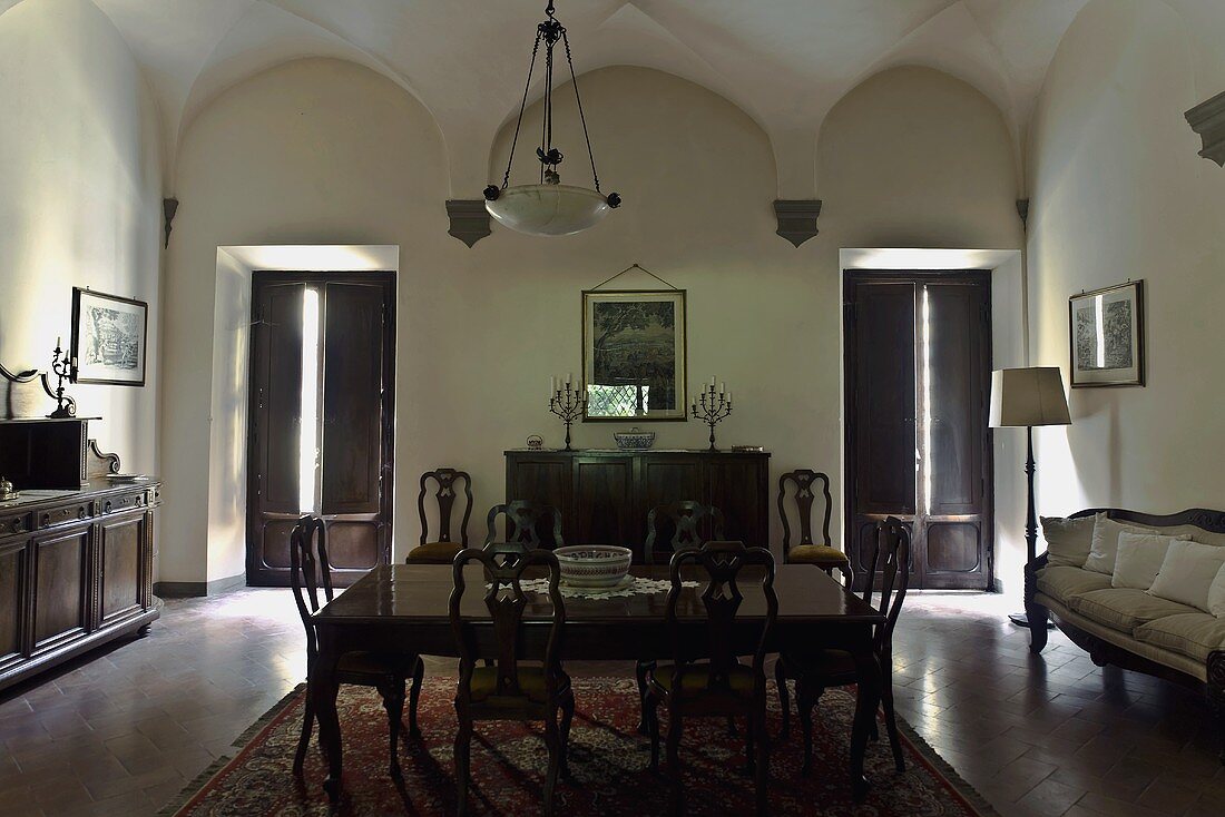 Vaulted ceiling in the darkened dining room of a villa with period furniture and windows with shutters