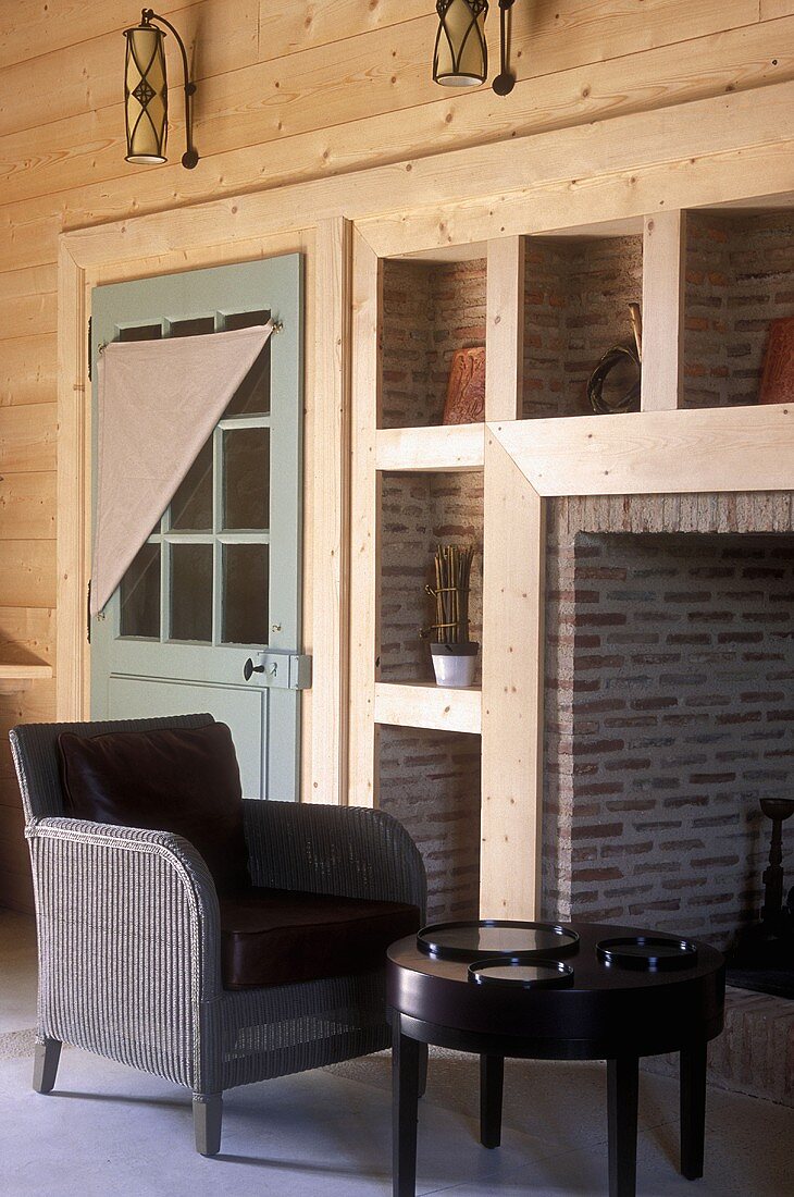 Country home with wood paneling in the living room, a wicker chair and table in front of the fireplace