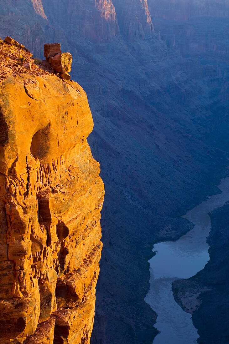 Golden sunrise light on boulder at the edge of a steep sheer rock cliff above the Colorado River, Toroweap, Grand Canyon National Park, Arizona