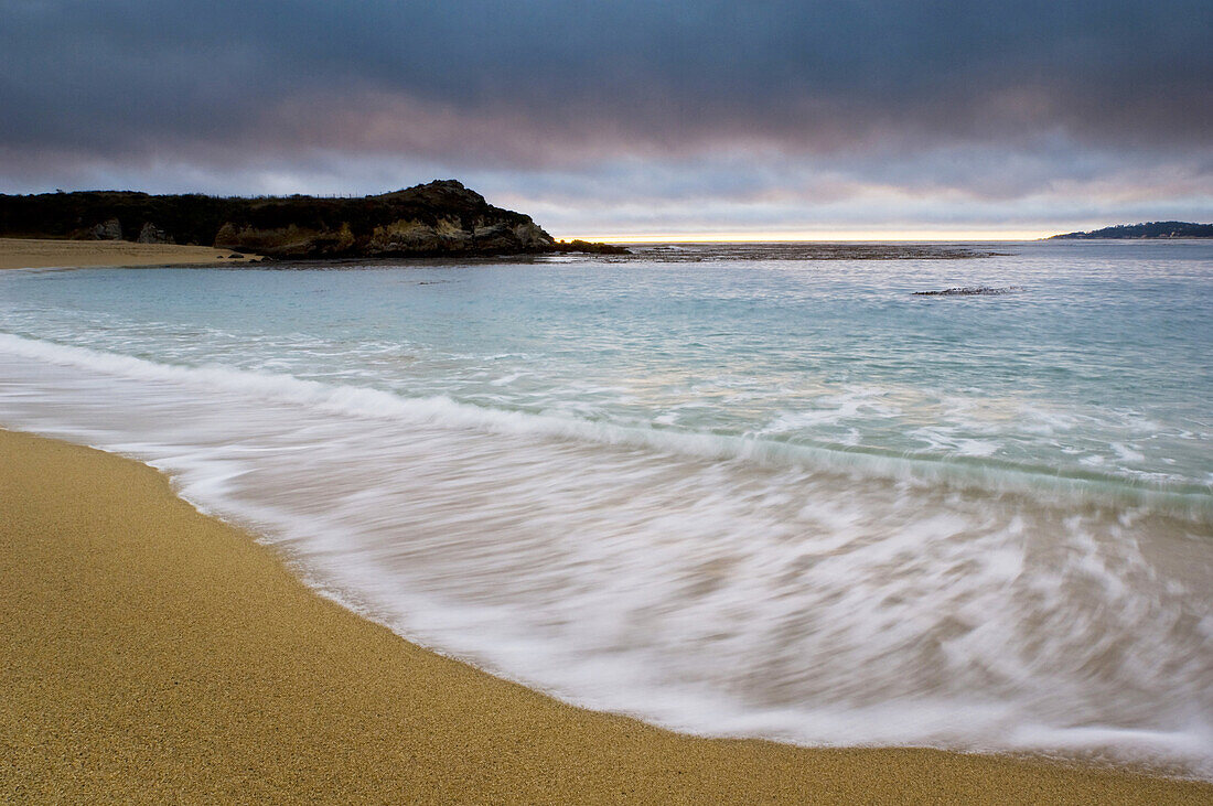 Waves breaking on sand beach at sunset, Carmel River State Beach, California.