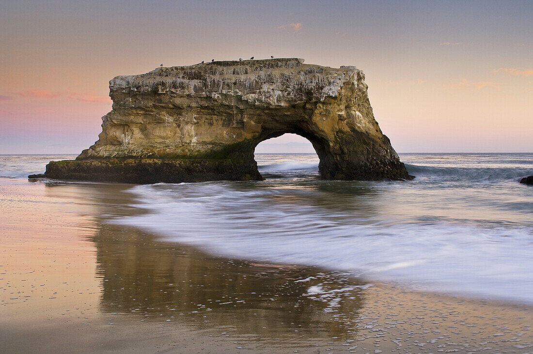 Arch rock and waves on sand beach in evening light, Santa Cruz, California.