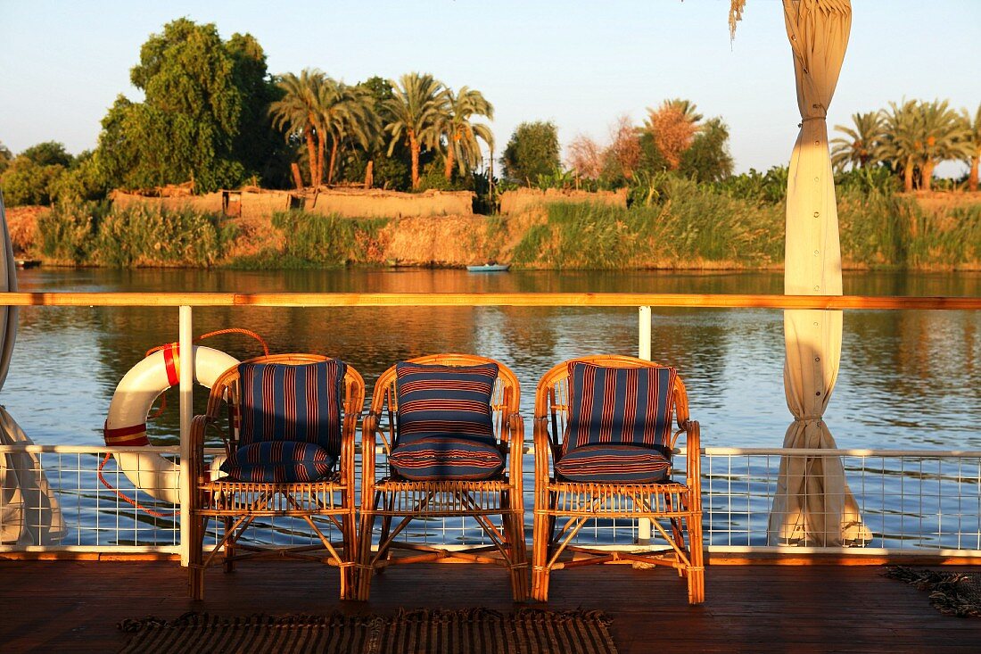 Abendstimmung auf Bootsdeck mit Korbstühlen vor der Reling und Dschungelblick, Nil, Ägypten