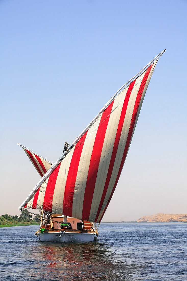 Segelboot mit rotweiss gestreiften Segeln auf dem Fluss, Nil, Ägypten