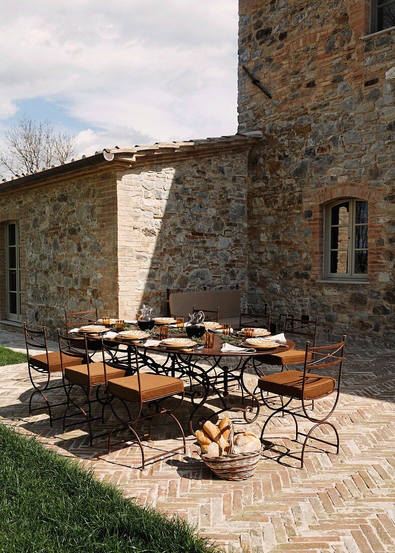 A table laid on a terrace in front of a Mediterranean country house and a stone floor with a herring bone pattern