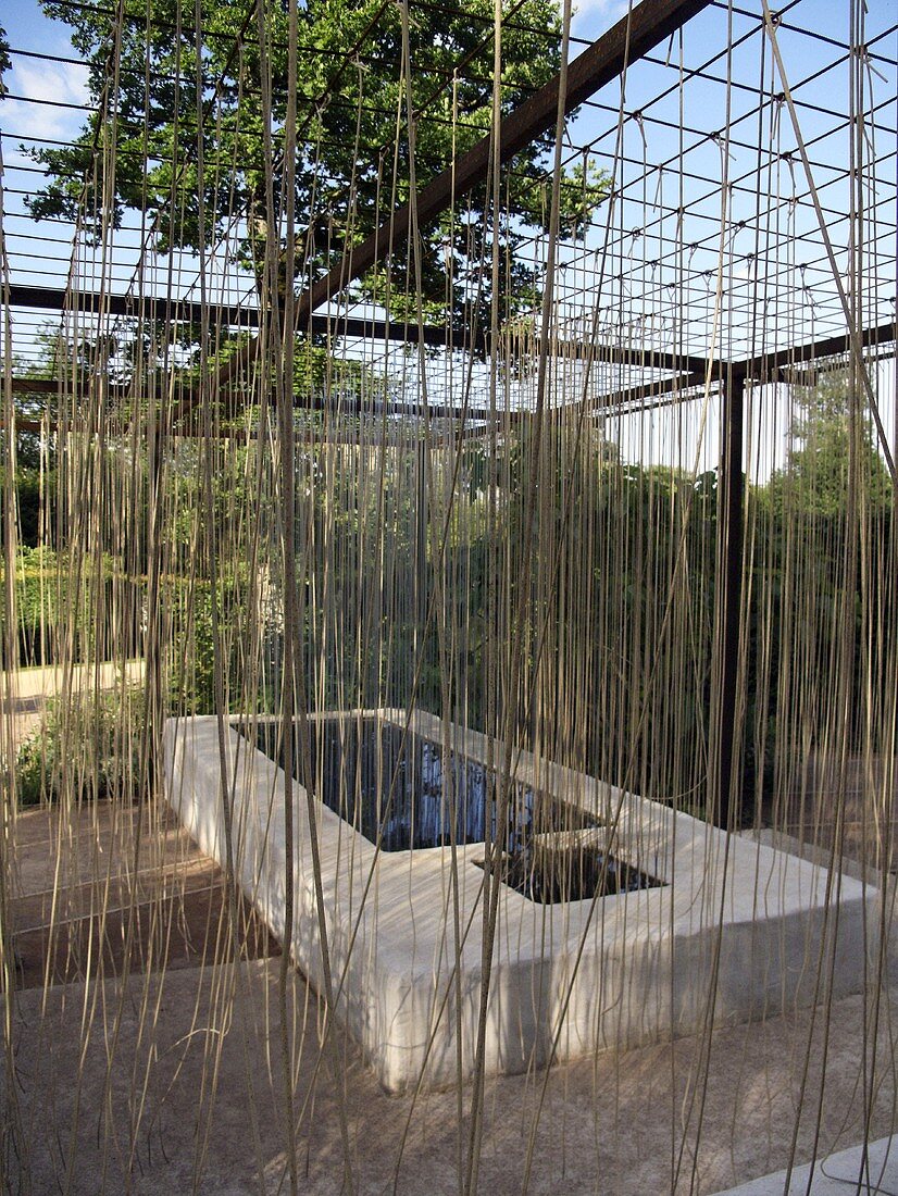 Künstlerische Gestaltung um ein Steinbecken mit Wasser unter der Pergola