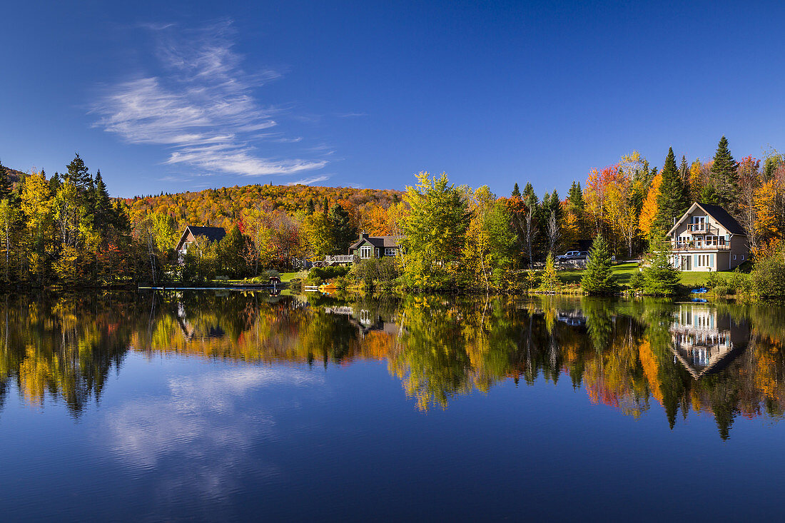Cottages and fall foliage color in the trees reflected in a calm lake at La Beauport, Quebec, Canada.