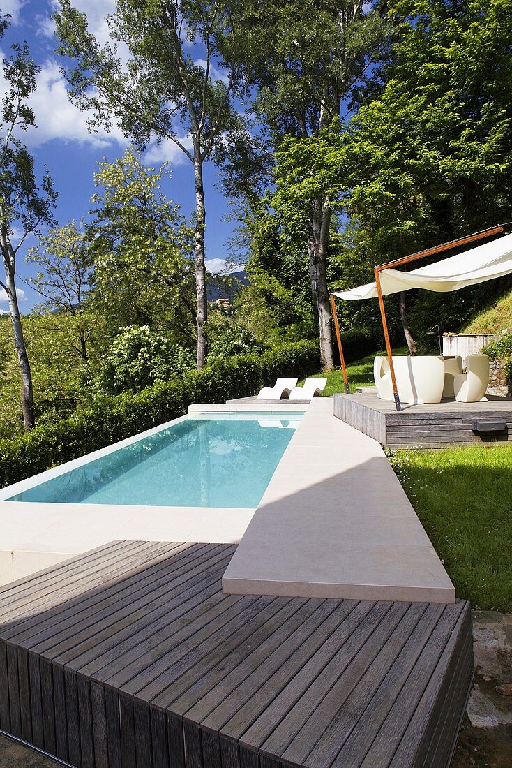 Turquoise water in a pool in a garden with a raised wooden platform and a stone footbridge