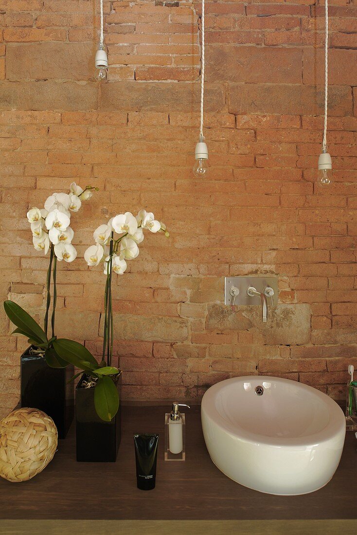 Vanity with a ceramic sink in front of a brick wall and white orchids in a vase