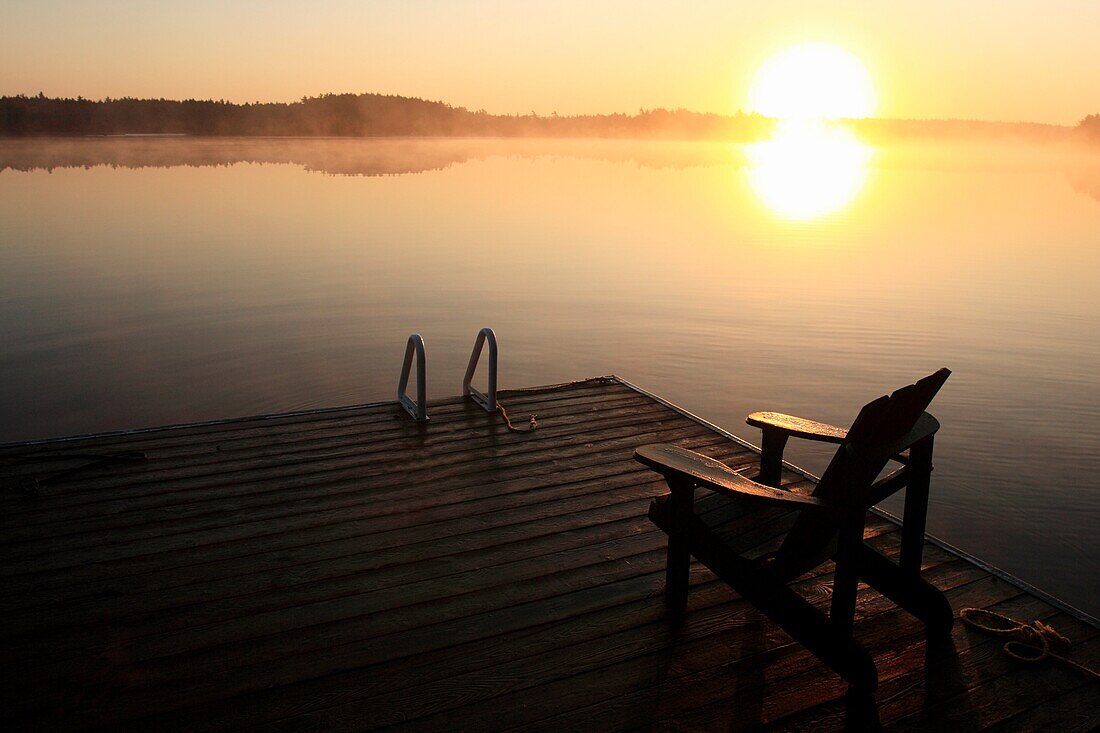 sunrise over a lake with a chair on a dock in the foreground