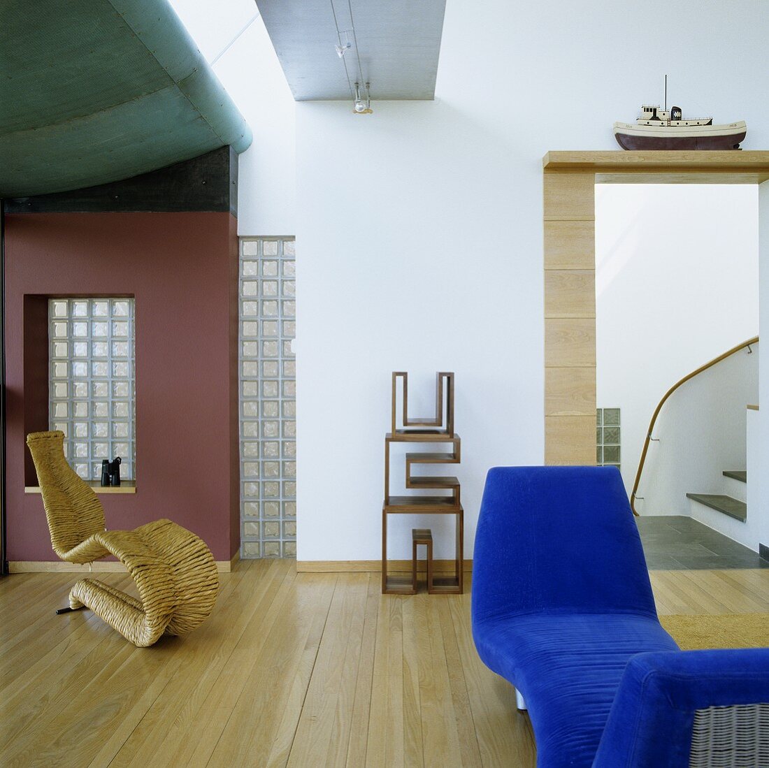 A blue divan and a designer wicker chair in front of a red wall in a living room