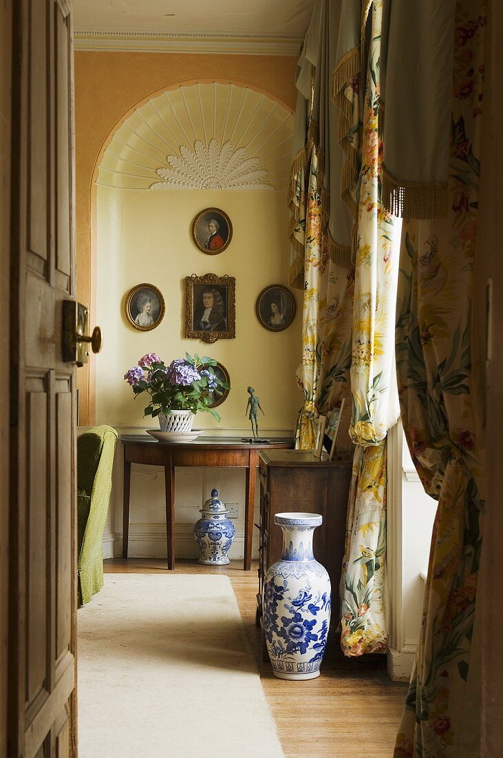 Blick durch offene Tür auf eine blau weiße Bodenvase und Beistelltisch vor gelbgetönter Wandnische