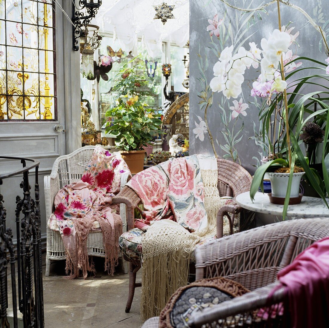 Wicker chairs with colourful throws and potted plants in a side room looking into a conservatory