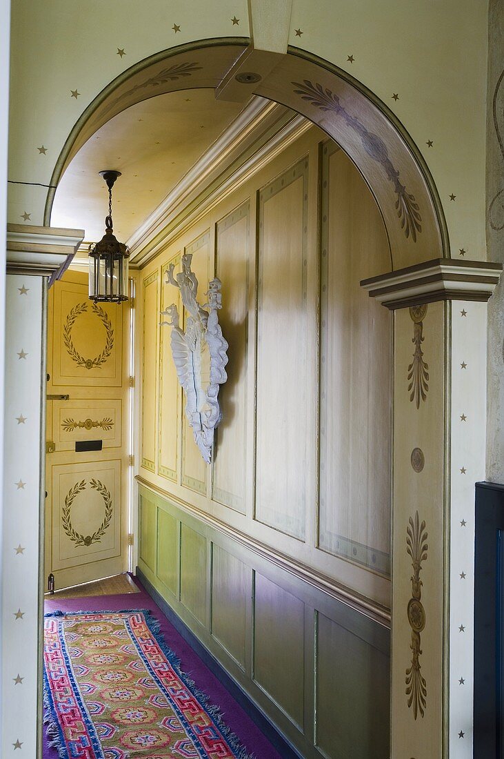 A view through a painted archway in a hallway with a wood panelled wall and an oriental rug