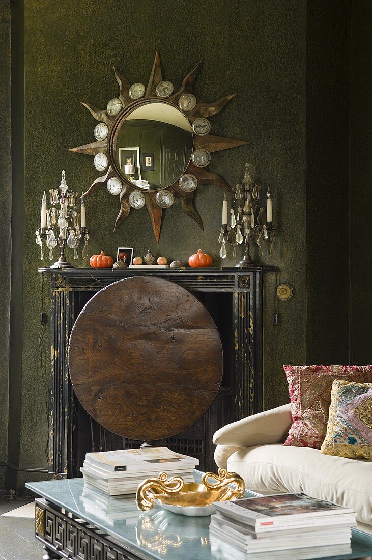 A metal disc in front of a fireplace and candle holders standing in front of a mirror in a star-shaped frame hung on a dark wooden wall