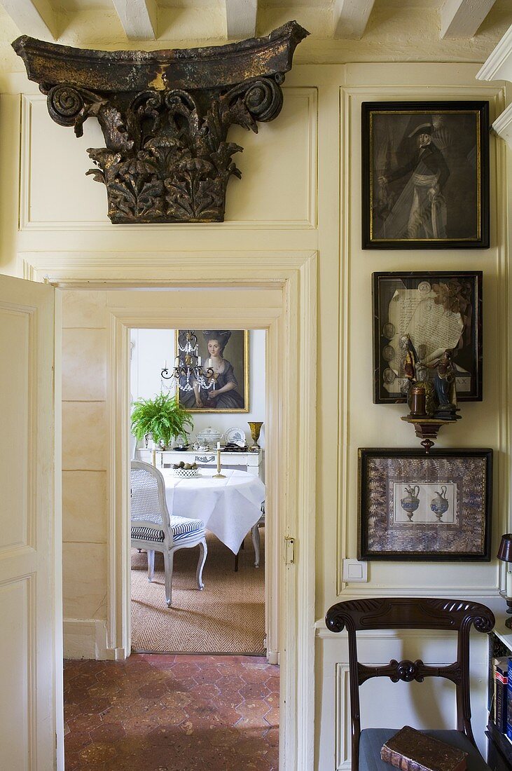 An antique Greek column capital above a door and view through an open door onto a dining room