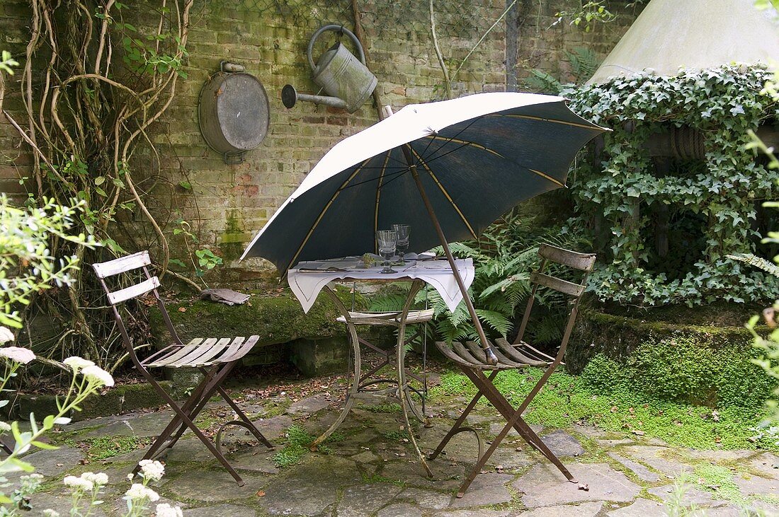 Alter Gartentisch mit Stühlen und Sonnenschirm auf Natursteinterrasse im Hinterhof