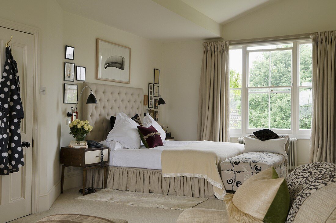 A spacious bedroom a high stack of light grey cushions on a double bed in front of a window