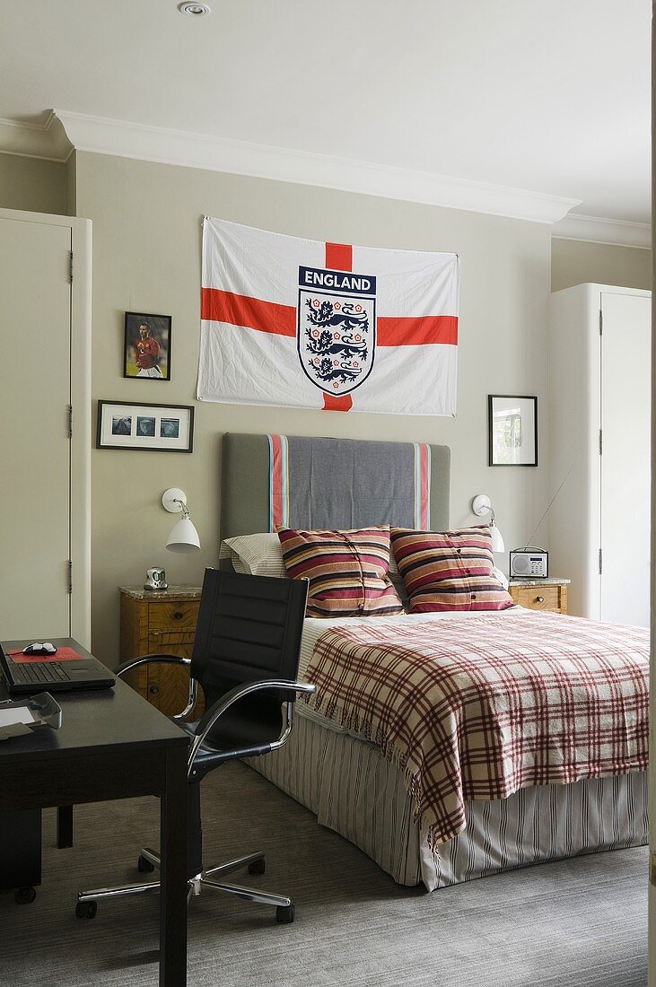 Jugendzimmer mit englische Nationalflagge über dem Bett und schwarzer Schreibtischstuhl vor Tisch
