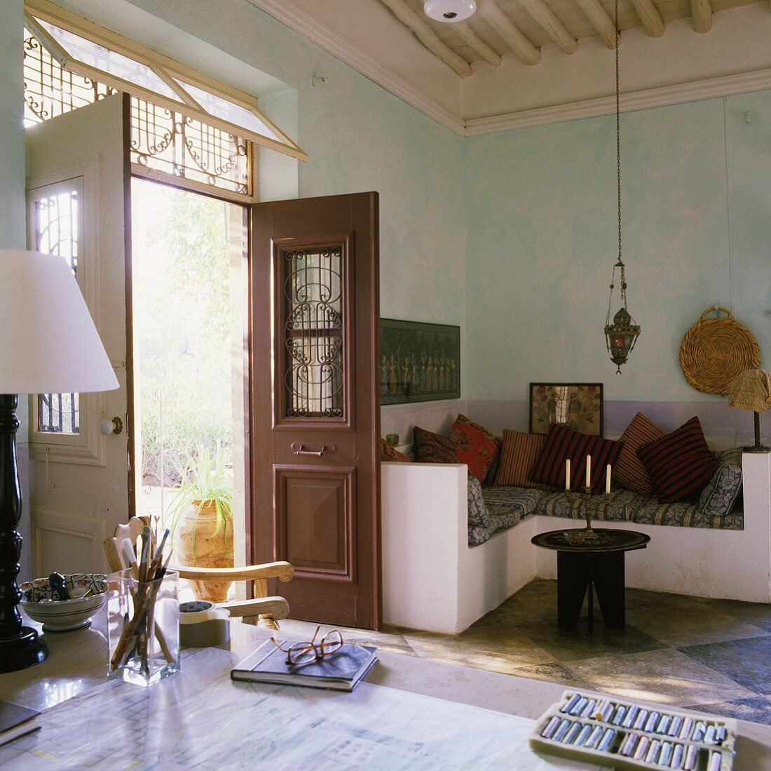 A living room in a Mediterranean house with a stone, upholstered seating corner and an open door with a view of the garden