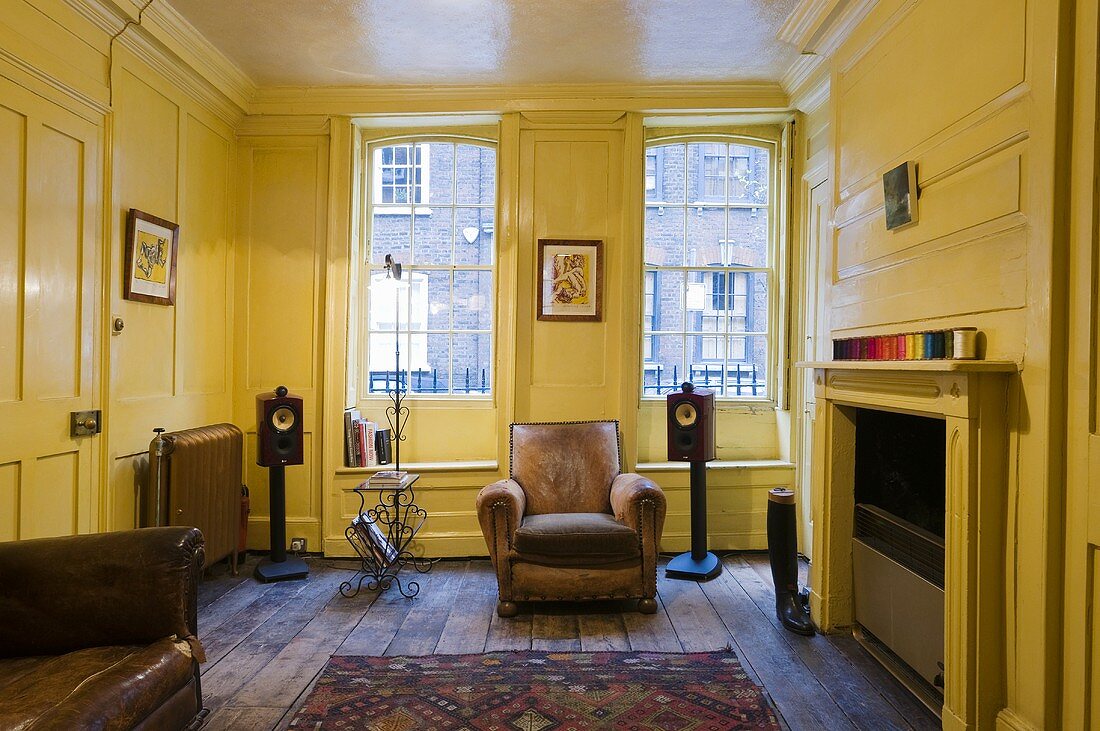 Yellow wood panelling in a living room with a fireplace and comfortable leather armchairs in front of the window