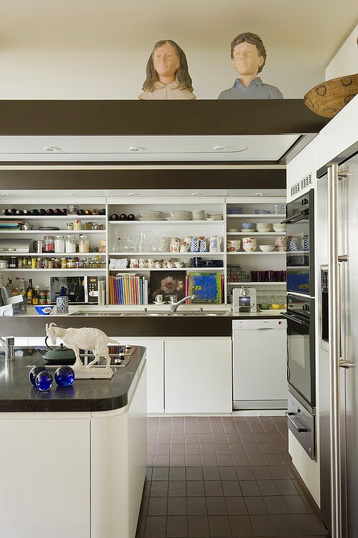 A white fitted kitchen with open shelving and wooden busts on the lowered ceiling