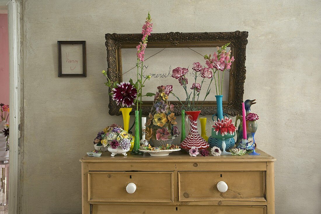 A colourful collection of vases on a wooden chest of drawers and a picture frame on a grey wall