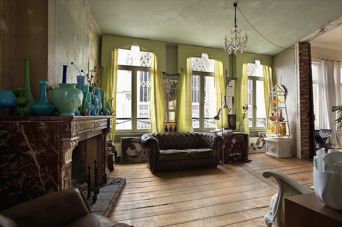 An old fireplace room with a leather sofa in front of a window hung with light grey, floor-length curtains