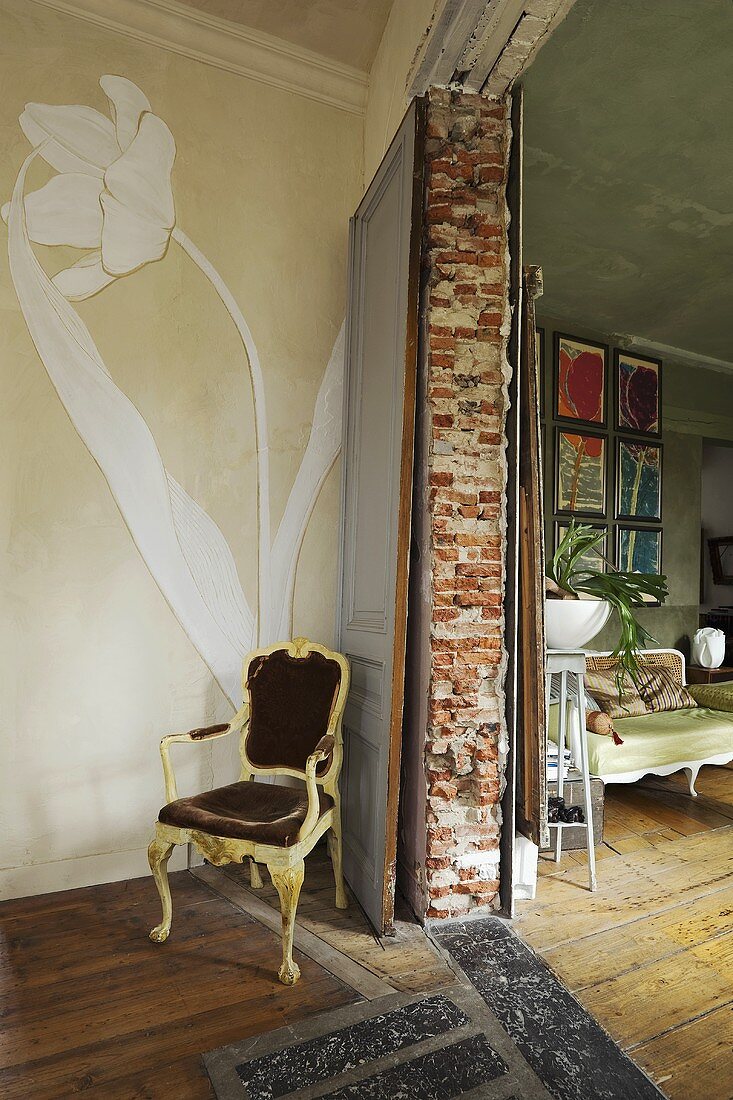 A worn chair and a flower painted on a wall next to a entrance into a living room