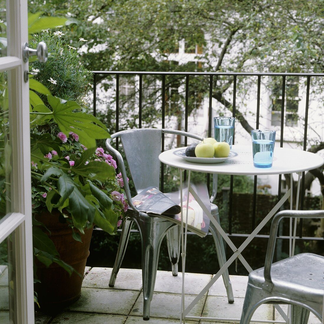 Metal chairs around a bistro table on a balcony with a garden view
