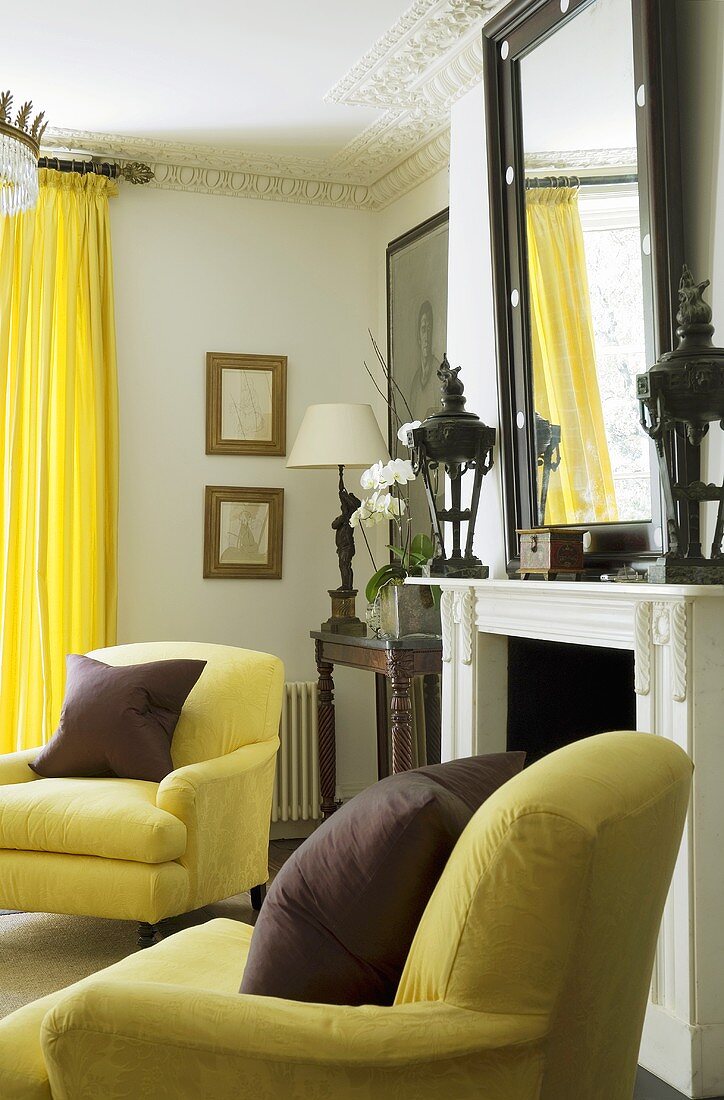 Dark red cushions on yellow armchairs in front of a fireplace with bright yellow curtains at the window
