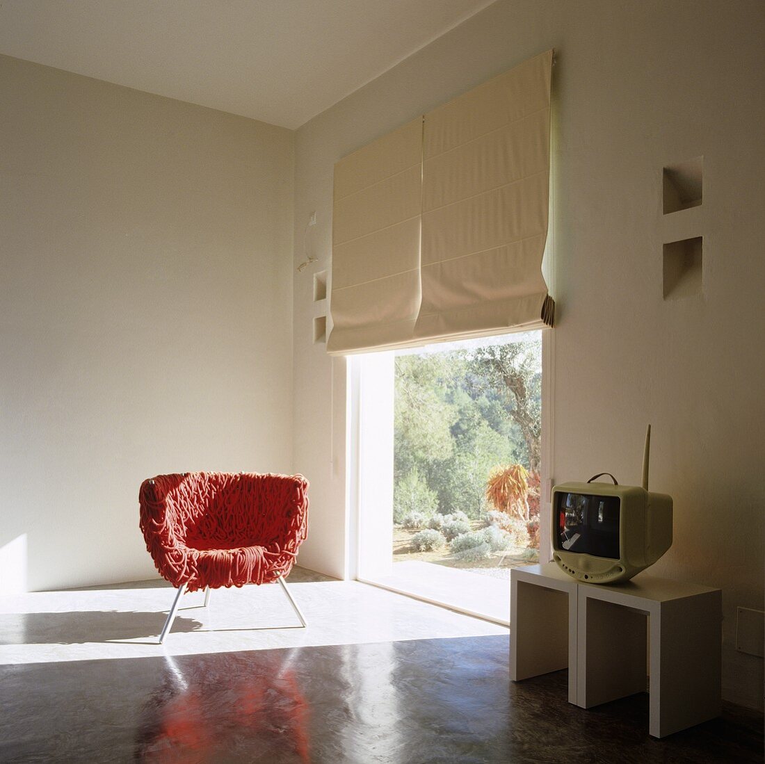 A red scraggy chair standing in a patch of light from a floor-to-ceiling window in a designer living room