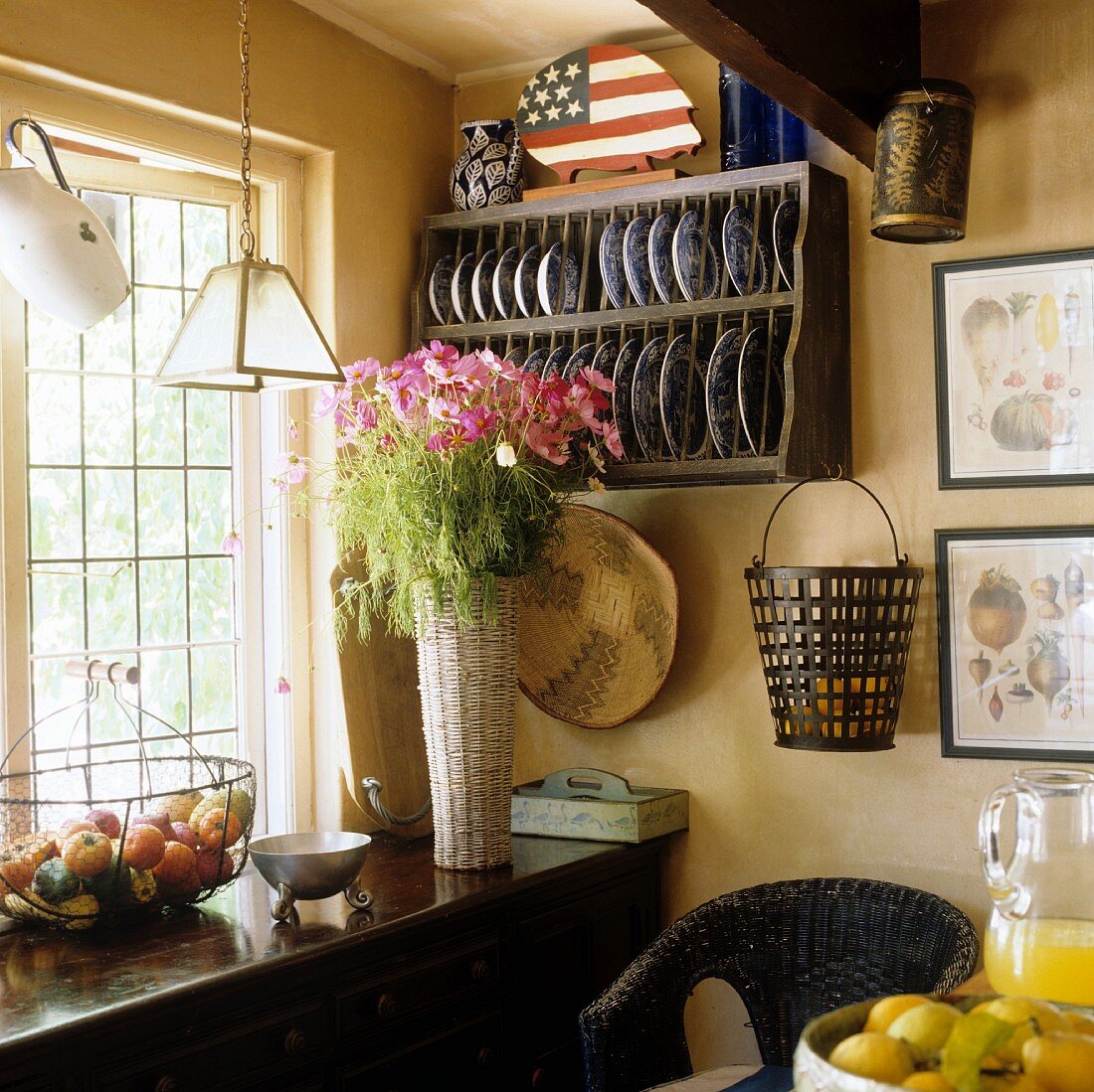 A corner of a kitchen with a plate rack and a bunch of flowers on a wooden shelf in front of the window