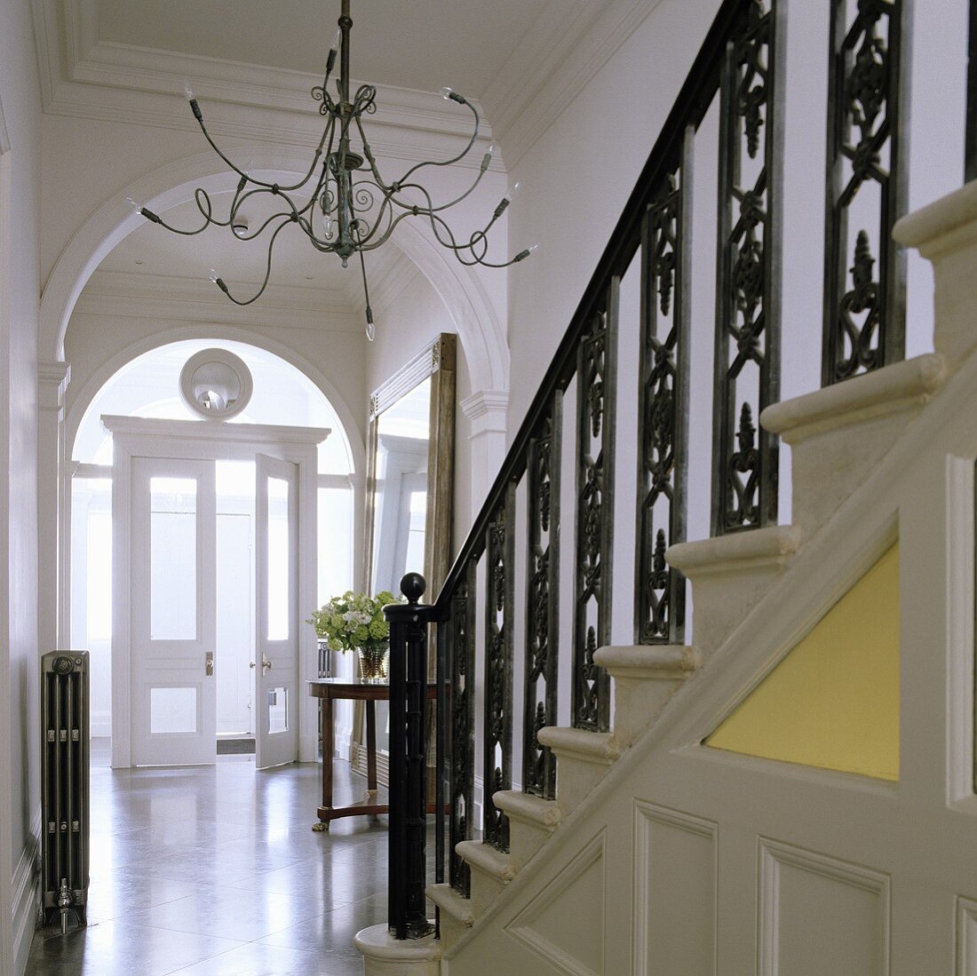 A flight of stairs with black, wrought iron banisters and a chandelier with Medusa arms in front of an archway