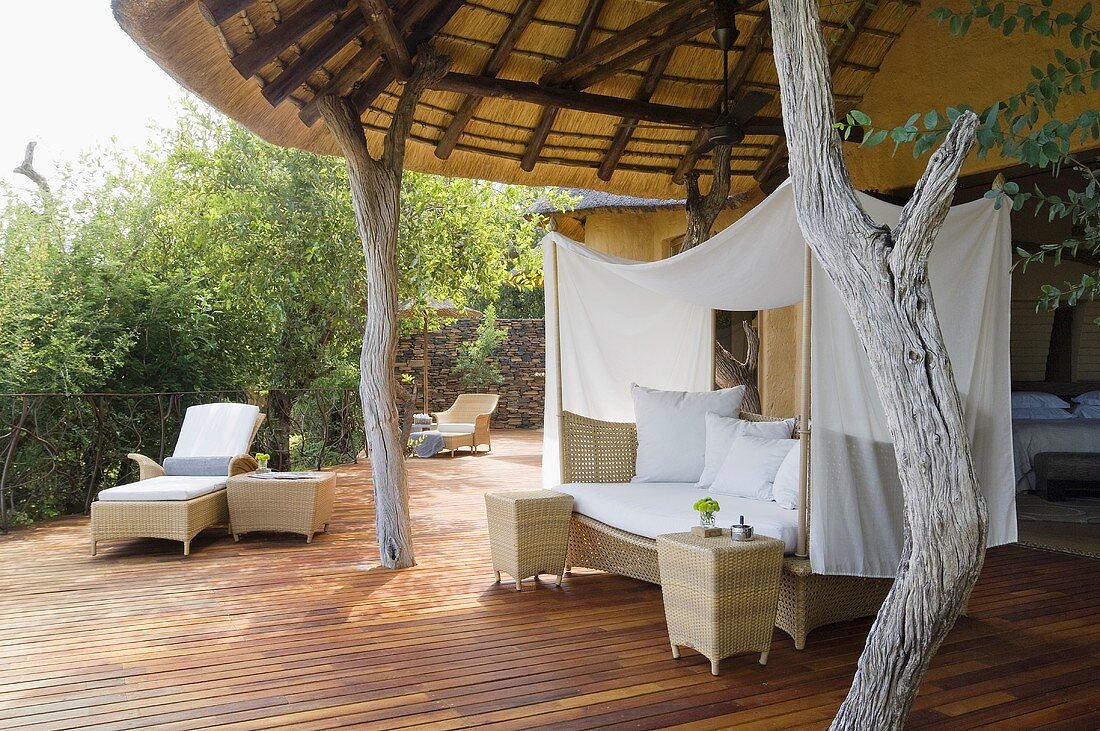 A wicker sofa with a white canopy and rustic wooden supports on the terrace of South African house