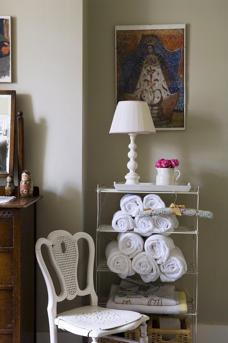 Alter Stuhl und Metallregal mit weisser Tischlampe und Handtüchern vor grauer Wand