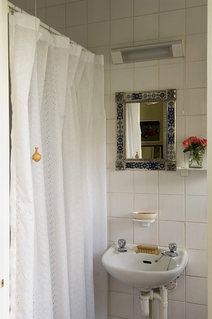 A wash basin and a mirror on a white tiled wall next to a close shower curtain
