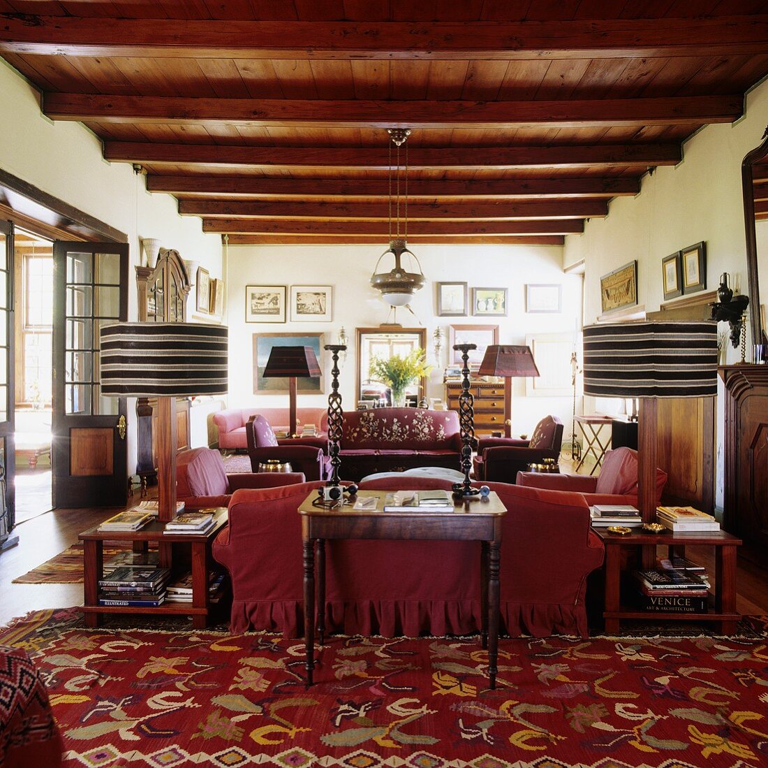 A living room with a rustic wood beam ceiling in a South African country house with a red sofa and table lamps with striped shades