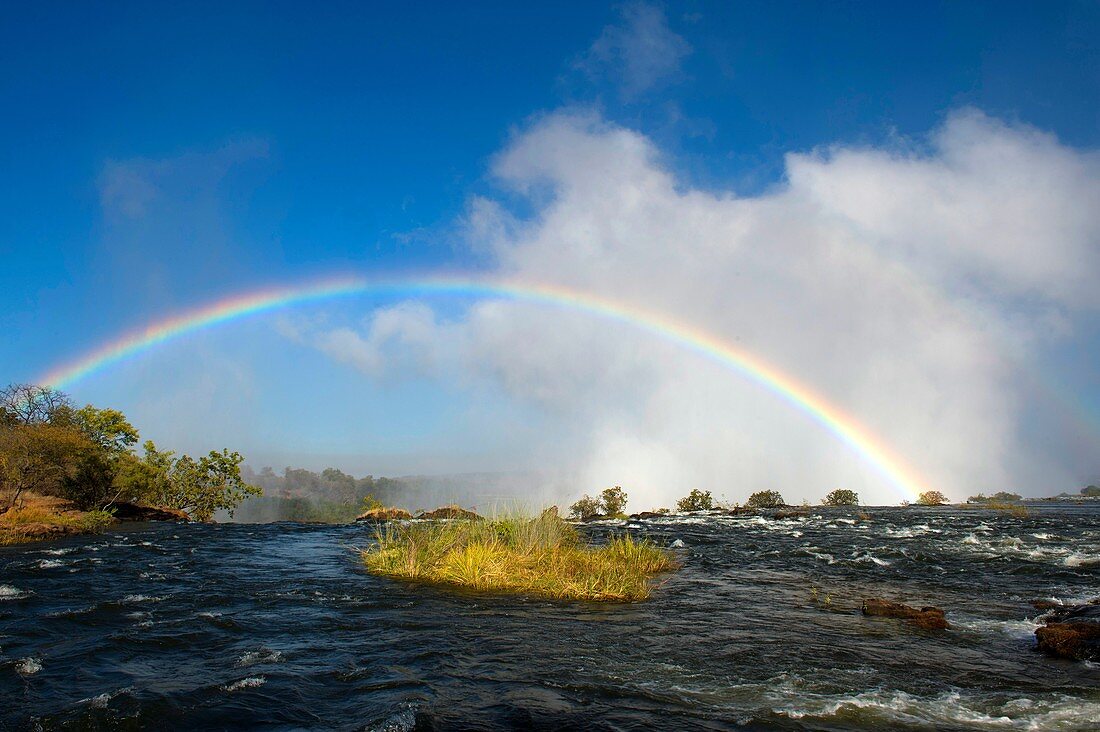 Rainbow over Victoria Falls seen from the shore of the Zambezi River at the section above the falls near Livingston in Zambia.