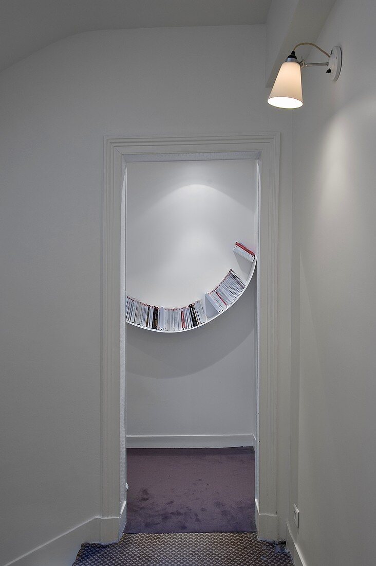 A view through an open door onto a curved bookshelf on a white wall