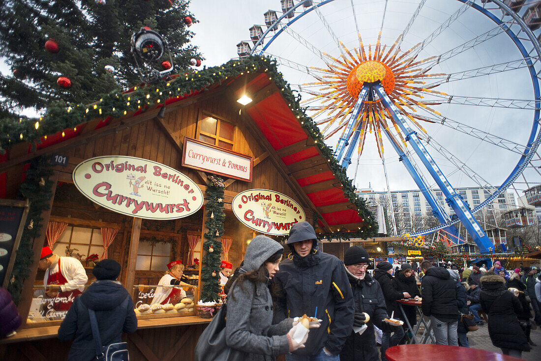 Ferris wheel and currywurst at the Christmas market in front of the Neptunbrunnen fountain, Alexanderplatz, Berlin. Snack Bar at Alexanderplatz. Bells, tinsel, carols, decorated trees? Christmas has definitely arrived. This special moment of the year star
